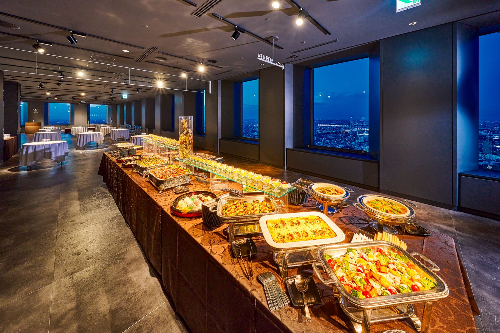 夜景を望む窓際に並ぶブッフェ料理と最大180名までの広々としたパーティー会場