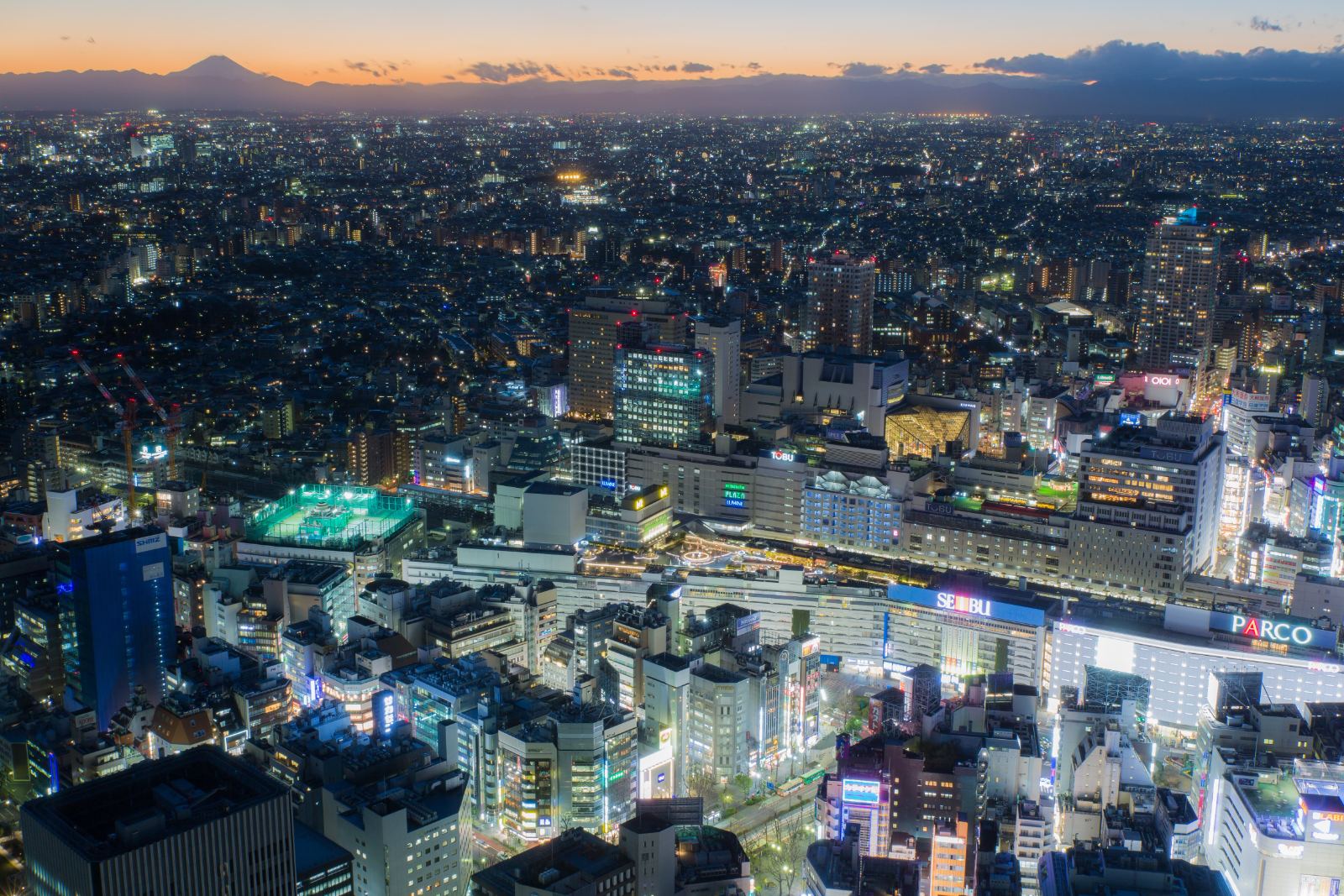 サンシャイン60展望台から望む360度の東京パノラマ夜景。夕暮れの空に富士山のシルエット、眼下に池袋の街明かりが広がる。